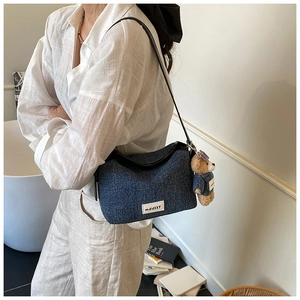 Detail of blue denim shoulder bag with cute bear plush charm and white textile label