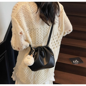 Close-up of black pleated leather bucket bag with drawstring and white pompom charm detail