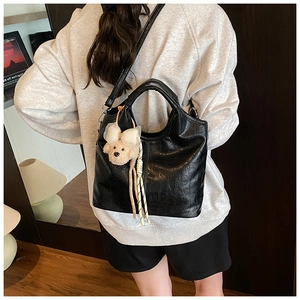 Detail of black crocodile texture bucket bag with a cute plush puppy pendant and strap