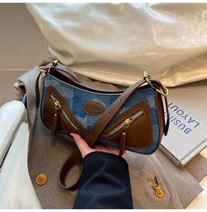 Detail of blue denim baguette bag with brown leather trim and decorative zippers