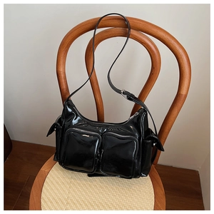 Close-up of black patent leather shoulder bag with vintage buckles and multi-pocket design