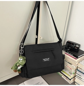 Detail of black messenger bag with flap zipper pocket and small green dinosaur charm