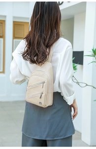 Rear view of a stylish beige crossbody bag for women on a model in an outdoor setting