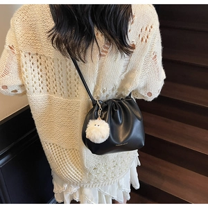 Detail of black leather drawstring bucket bag with plush charm and golden logo text