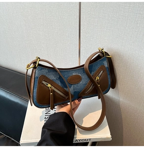 Detail view of denim fabric baguette bag with leather trim and gold zippers