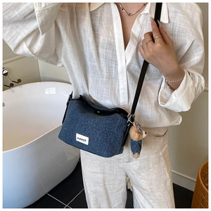 Detail of blue denim bucket bag with mddl37 label, leather strap and teddy bear charm