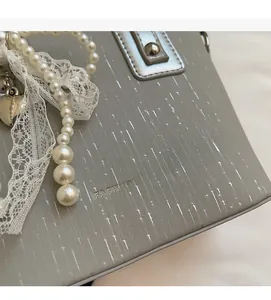 Detailed close-up of grey handbag with pearls, lace trim, and silver heart charm pendant