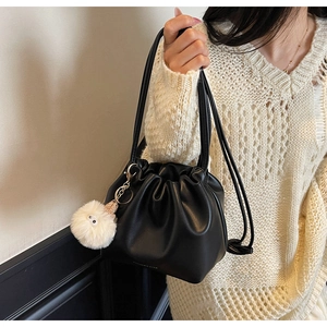 Detail of black pleated bucket bag featuring a white faux fur charm with eyes