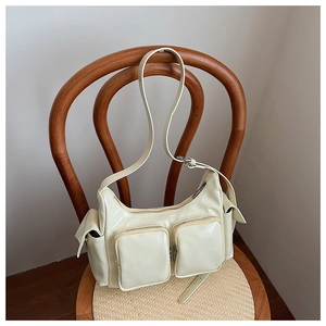 Detail of beige glossy leather shoulder bag with functional multi-pocket design on wood chair