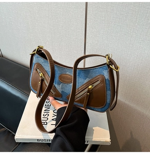 Detailed close-up of retro denim baguette bag with brown leather trim and zipper accents