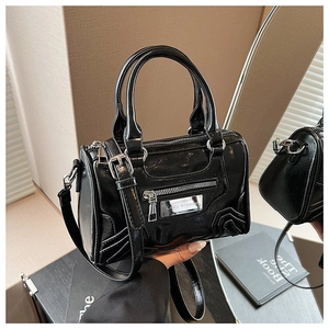 Detalle de bolso Boston en charol negro con cremallera metálica y placa plateada