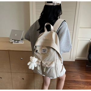 Dettaglio dello zaino in tela beige con toppa waswac e ciondolo a forma di orsetto