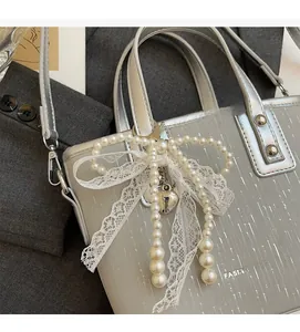 Close-up of silver tote bag with pearl lace bow and metal heart charm detail