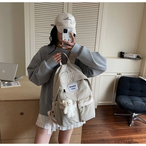 Dettaglio dello zaino in tela beige con tasche multiple e un ciondolo a forma di orsetto