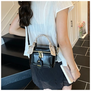 Détail d'un sac boîte noir brillant avec ferrures dorées et poignée ornée d'un foulard