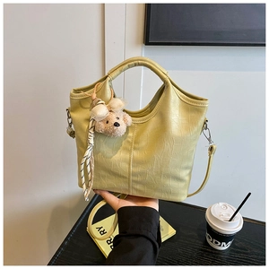 Detail of light green crocodile embossed bucket bag with plush bear and silk scarf charms