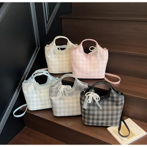 Detail of five plaid tote bags with pearl and lace bow charms on wooden stairs
