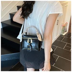 Detail of a black leather crossbody bucket bag featuring a silk scarf wrap and gold hardware