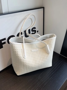 Elegant beige woven tote bag with leather trim and shoulder straps on a wooden surface