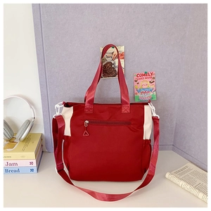 Detail view of red and white nylon tote bag with adjustable strap and front zipper pocket