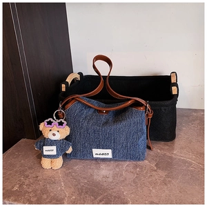 Close-up of denim bucket bag with brown leather handles and cute teddy bear pendant