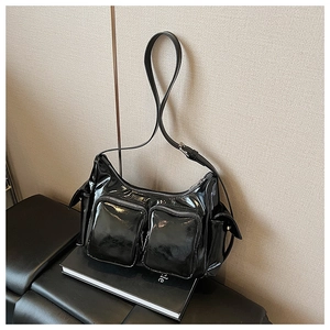 Close-up of black patent leather crossbody bag with dual zipper pockets and silver hardware