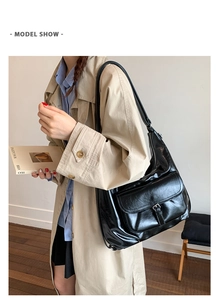 Nahaufnahme der schwarzen Leder-Hobo-Tasche mit Schnallentasche auf einem beigen Trenchcoat