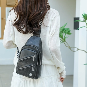 Detail of a black matte crossbody bag with three zipper pockets and a patterned strap