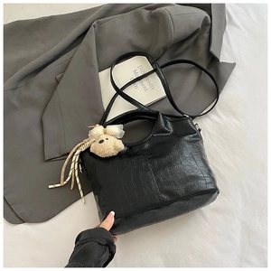 Detail of black crocodile texture handbag with plush bear charm and tassel on a suit