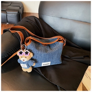 Detail of blue denim bucket bag with brown leather handles and a plush bear pendant