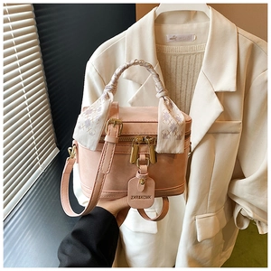 Détail du sac boîte en cuir rose avec poignée tressée, foulard et finitions dorées