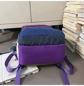 Close-up of color-block nylon backpack featuring plush cat charm and purple woven straps