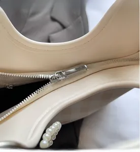 Detail view of smooth metal zipper and pearl decoration on a cream checkered handbag