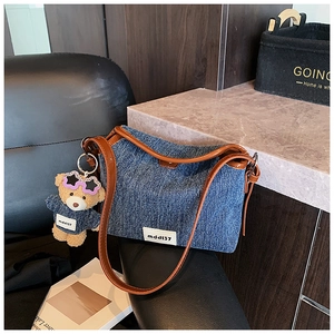 Detail view of denim shoulder bag with brown leather handles and a plush bear charm