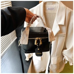 Detail of black box handbag with gold hardware and a decorative beige silk scarf handle