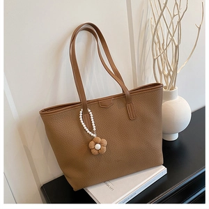 Détail d'un sac cabas en cuir grainé marron avec fleur tissée et breloque en perles