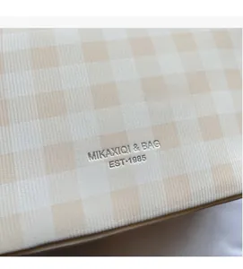 Detail of checkered beige tote bag featuring silver embossed MIKAXIQI & BAG logo lettering