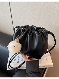 Chic black pleated bucket bag with long strap and a cute white fuzzy monster charm