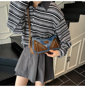 Detail of color-block denim crossbody bag featuring leather trim and dual zip pockets