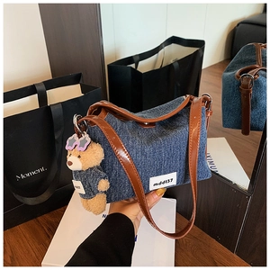 Detail of blue denim bucket bag with brown leather strap and teddy bear charm