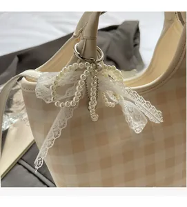 Detail of beige checkered tote bag featuring pearl chain and lace bow decoration