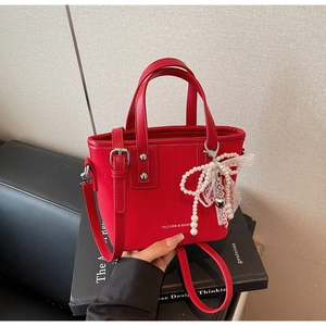 Detail of red leather tote bag with a pearl lace bow charm and adjustable strap