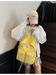Zaino in tela giallo acceso con design multitasca indossato da modella in stile minimalista