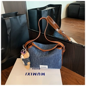 Close-up of denim bucket bag with brown leather trim and a cute plush bear charm