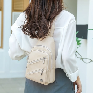 Outdoor view of a beige crossbody bag featuring a wide strap and dual front zippers