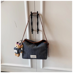 Detail of a blue denim bucket bag with brown leather trim and a cute teddy bear charm