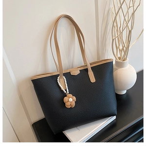Détail d'un cabas en cuir noir grainé avec chaîne de perles et breloque fleur