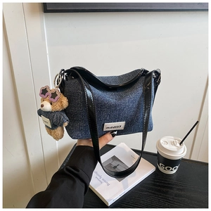 Close-up of denim shoulder bag with black patent leather trim and a plush bear charm