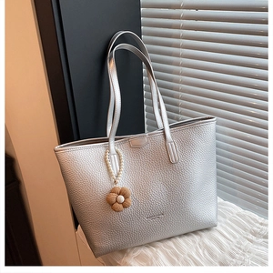 Détail du cabas en cuir grainé argenté avec breloque en perles sous une lumière naturelle
