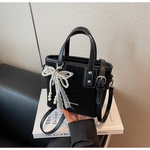 Detail of black textured tote bag with silver studs and pearl lace bow pendant accessory